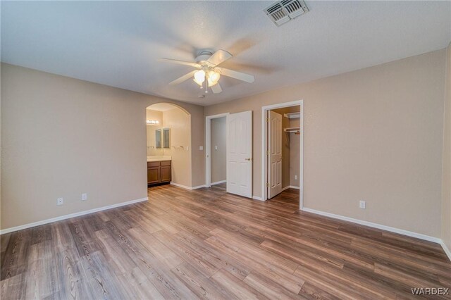 unfurnished bedroom featuring arched walkways, wood finished floors, visible vents, and baseboards