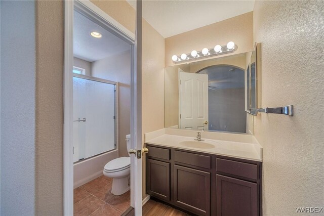 full bathroom featuring shower / bath combination with glass door, a textured wall, toilet, vanity, and tile patterned flooring