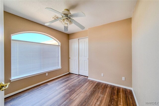 unfurnished bedroom with baseboards, visible vents, ceiling fan, wood finished floors, and a closet