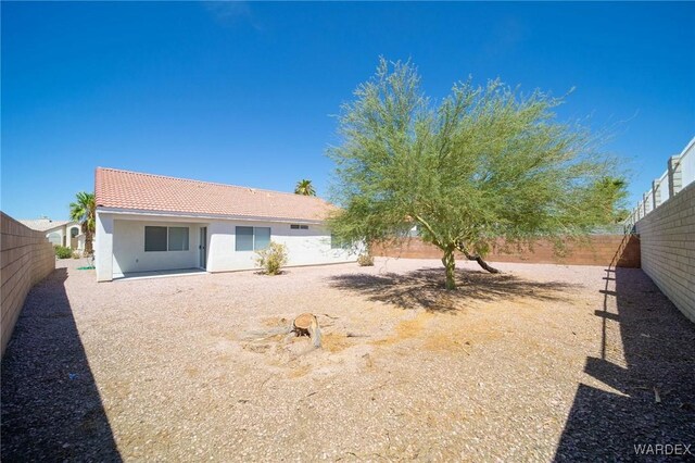 rear view of property featuring a tile roof, a fenced backyard, and stucco siding