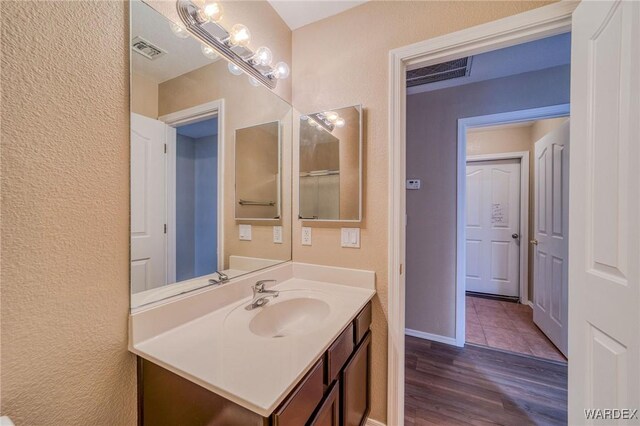 bathroom with visible vents, vanity, baseboards, and wood finished floors