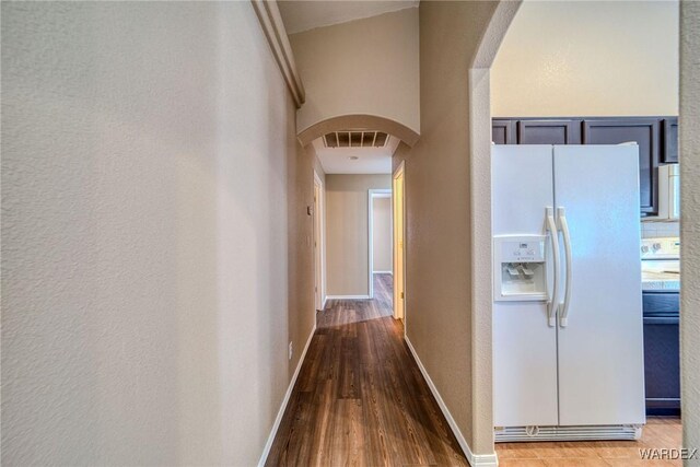 corridor with arched walkways, visible vents, baseboards, and wood finished floors