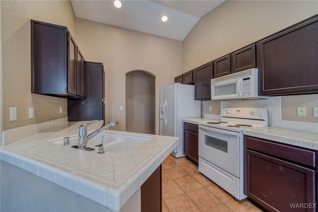 kitchen featuring tile counters, a sink, dark brown cabinetry, white appliances, and a peninsula