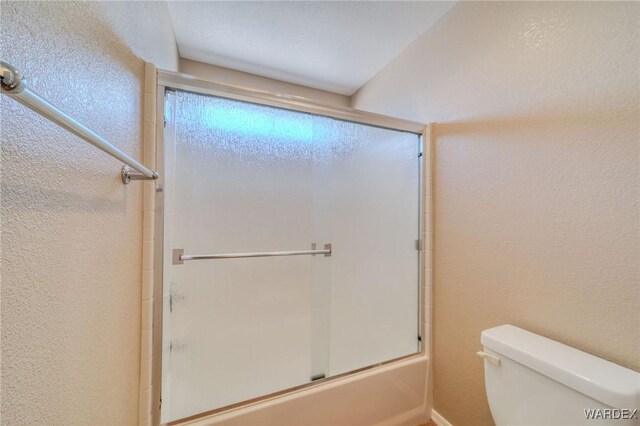 full bath with toilet, enclosed tub / shower combo, and a textured wall