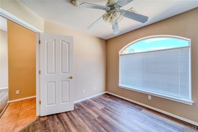 empty room with a ceiling fan, a textured ceiling, baseboards, and wood finished floors