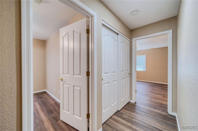 corridor featuring a textured wall, dark wood-style flooring, and baseboards