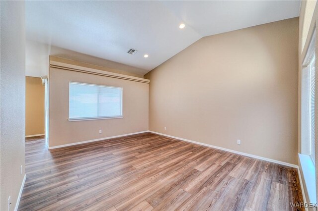 spare room featuring baseboards, visible vents, vaulted ceiling, and wood finished floors