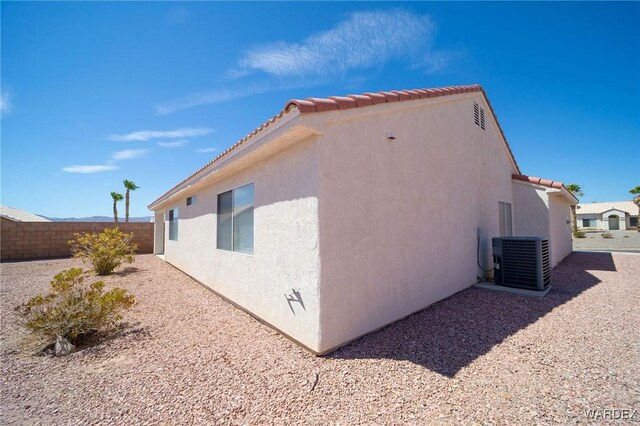 view of home's exterior featuring central AC, fence, a tiled roof, and stucco siding