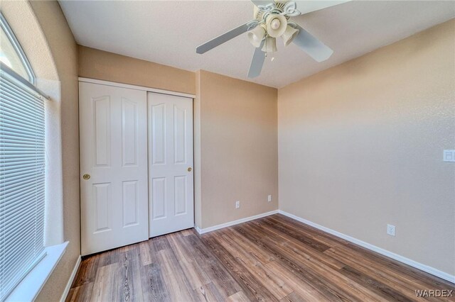 unfurnished bedroom with a ceiling fan, a closet, baseboards, and wood finished floors