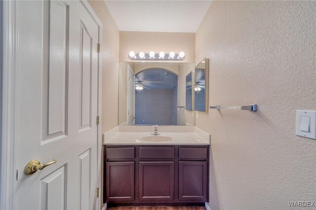 bathroom featuring ceiling fan, a textured wall, and vanity