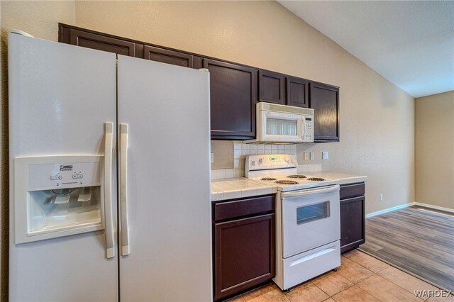 kitchen featuring lofted ceiling, light tile patterned floors, white appliances, dark brown cabinets, and decorative backsplash