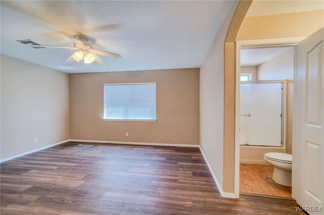 unfurnished bedroom with baseboards, visible vents, dark wood-type flooring, ensuite bathroom, and a textured ceiling