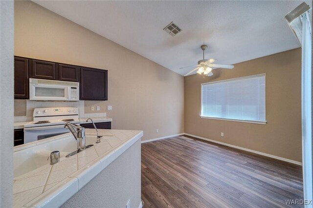 kitchen with dark wood-style flooring, visible vents, vaulted ceiling, dark brown cabinetry, and white appliances