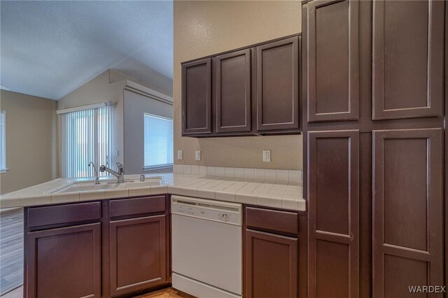 kitchen featuring dishwasher, tile countertops, a peninsula, and a sink