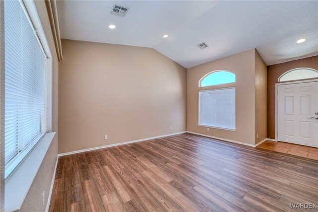 foyer with visible vents, vaulted ceiling, baseboards, and wood finished floors