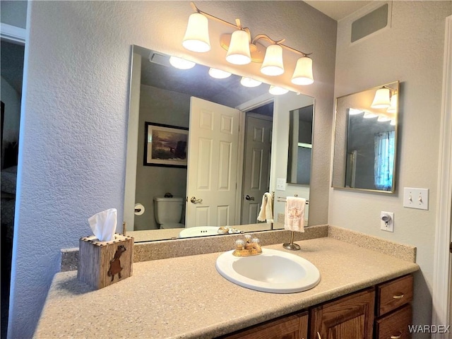 bathroom featuring a textured wall, vanity, visible vents, and toilet