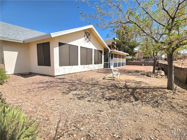 rear view of property featuring a sunroom, stucco siding, and fence