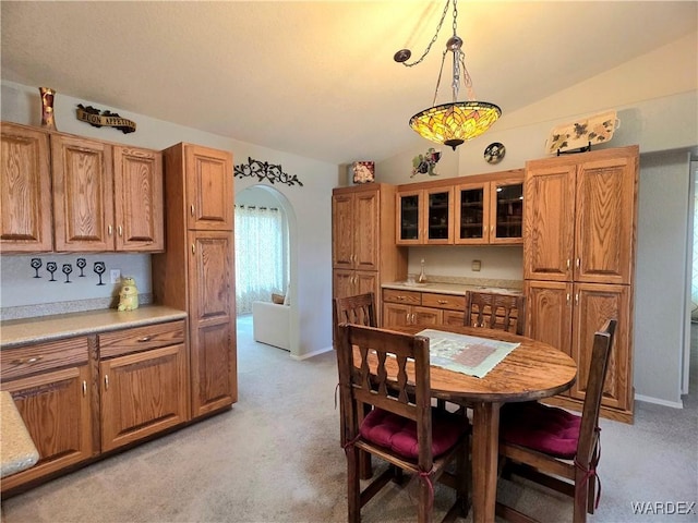 dining room featuring arched walkways, light colored carpet, baseboards, and vaulted ceiling