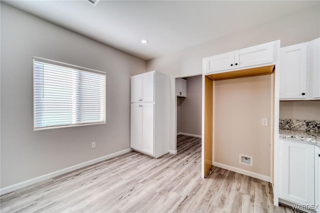 kitchen featuring light wood-style floors, baseboards, light stone counters, and white cabinets