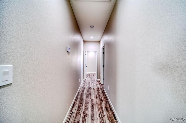 hallway with a textured wall, wood finished floors, and baseboards