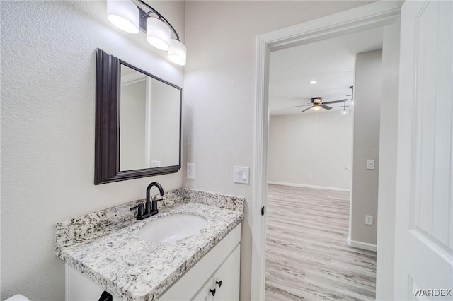 half bath featuring ceiling fan, vanity, baseboards, and wood finished floors