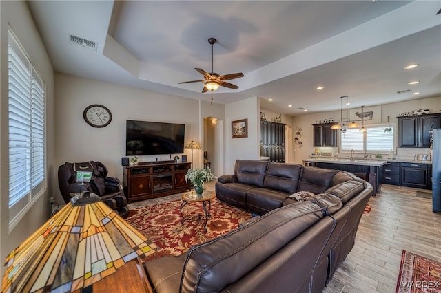 living room featuring light wood finished floors, visible vents, arched walkways, a tray ceiling, and recessed lighting