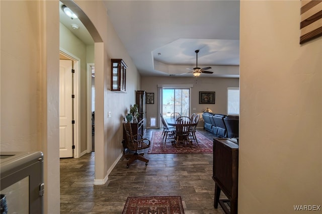 entryway with arched walkways, ceiling fan, a raised ceiling, and baseboards