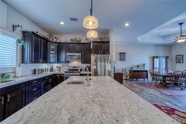 kitchen featuring decorative light fixtures, appliances with stainless steel finishes, a sink, dark brown cabinets, and light stone countertops