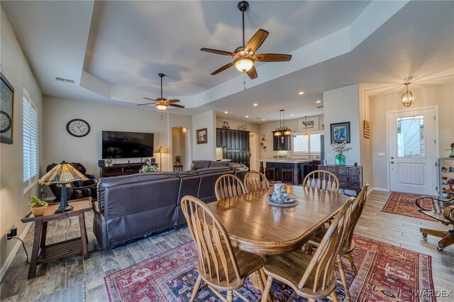 dining area with baseboards, visible vents, a ceiling fan, a raised ceiling, and wood finished floors