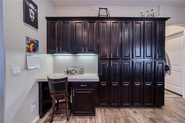 kitchen featuring dark brown cabinetry, arched walkways, and light wood finished floors