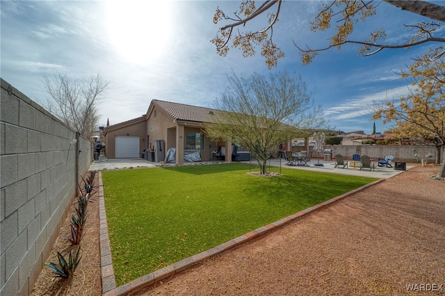 back of house featuring a yard, stucco siding, a patio area, a garage, and a fenced backyard