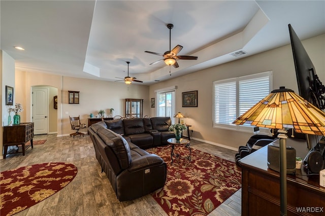 living area with arched walkways, visible vents, baseboards, light wood finished floors, and a raised ceiling