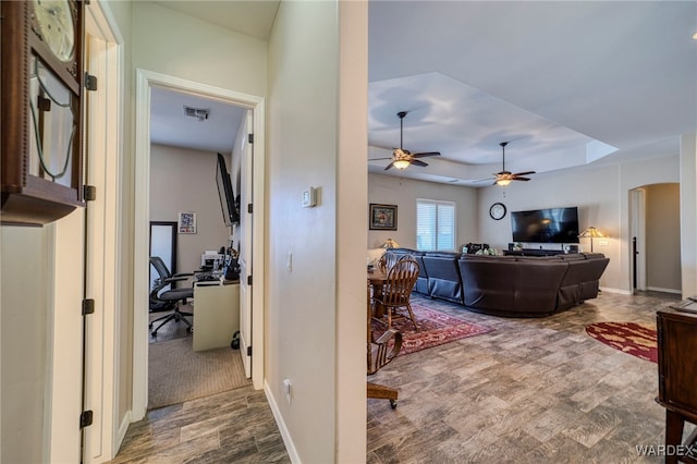 living room with visible vents, arched walkways, a raised ceiling, baseboards, and ceiling fan