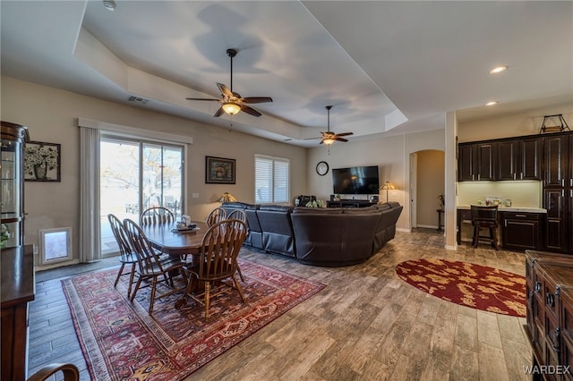 dining area with visible vents, arched walkways, a tray ceiling, light wood-style floors, and recessed lighting