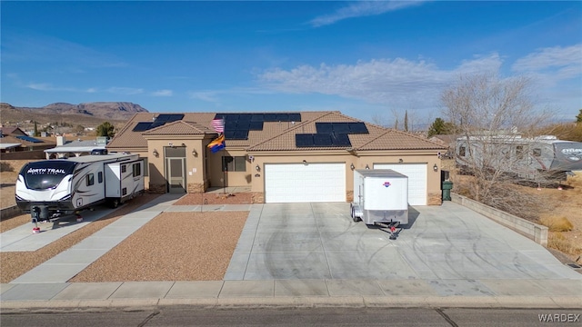 mediterranean / spanish-style house featuring solar panels, a tile roof, an attached garage, a mountain view, and stucco siding