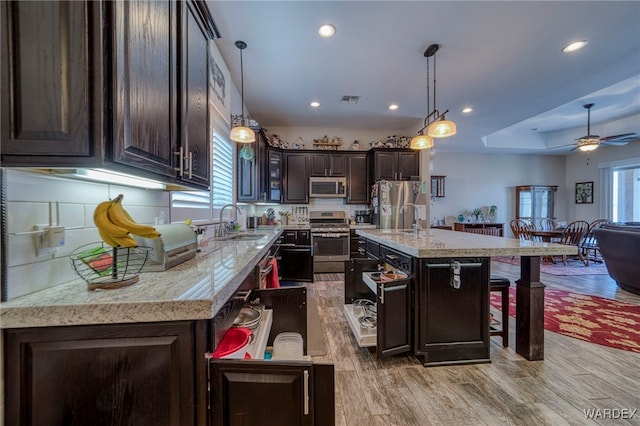 kitchen with stainless steel appliances, hanging light fixtures, a kitchen island with sink, and dark brown cabinets