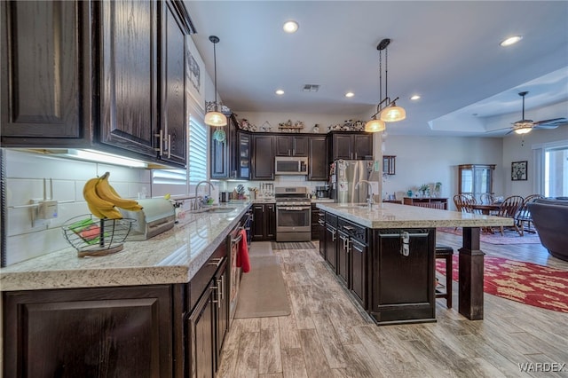 kitchen with dark brown cabinets, appliances with stainless steel finishes, a center island with sink, and pendant lighting