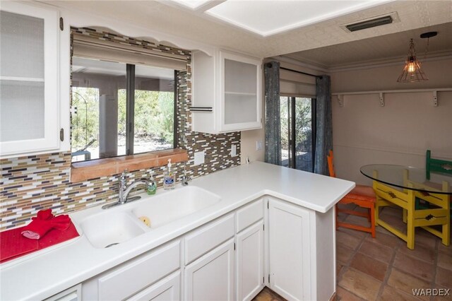 kitchen featuring white cabinets, visible vents, a sink, glass insert cabinets, and tasteful backsplash