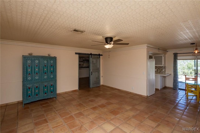 unfurnished room featuring baseboards, visible vents, ceiling fan, and a barn door