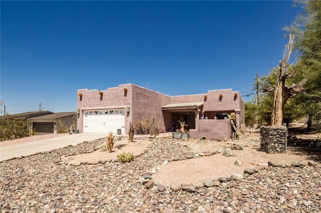 pueblo revival-style home with an attached garage, concrete driveway, and stucco siding