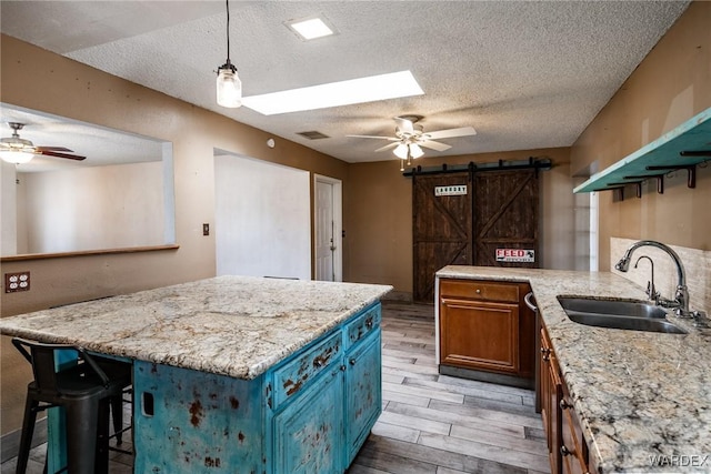 kitchen with a barn door, light wood-style flooring, blue cabinets, a peninsula, and a sink