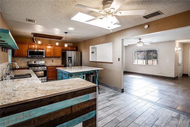 kitchen with visible vents, appliances with stainless steel finishes, brown cabinets, a textured ceiling, and a sink