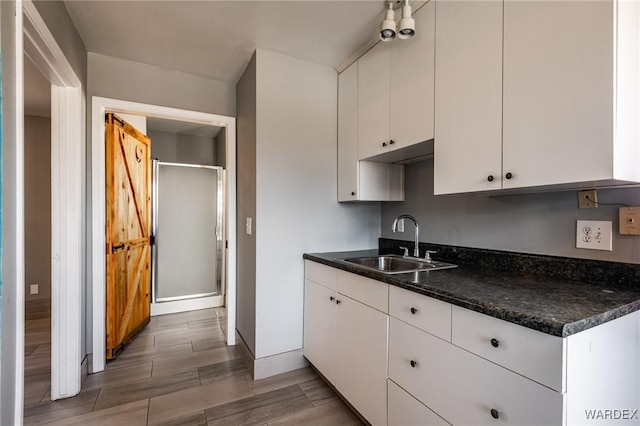 kitchen with baseboards, white cabinets, dark countertops, wood tiled floor, and a sink