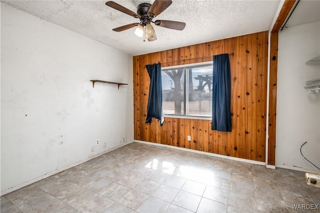 unfurnished room with a ceiling fan, baseboards, wooden walls, and a textured ceiling