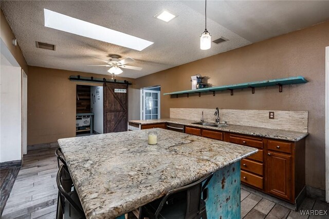 kitchen featuring a barn door, a skylight, a sink, open shelves, and brown cabinetry