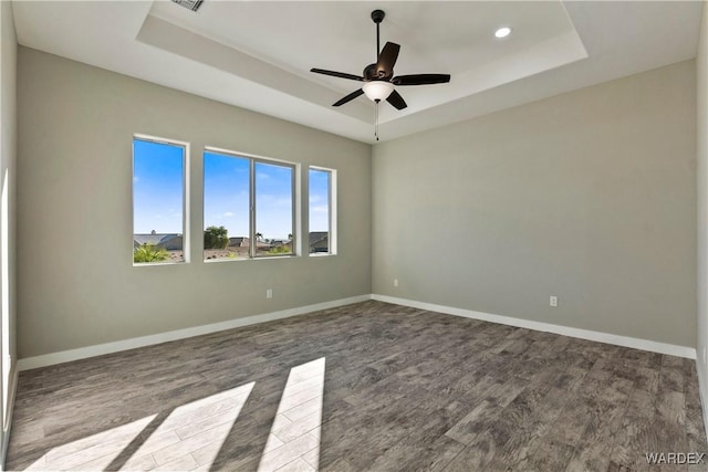 empty room featuring ceiling fan, baseboards, a raised ceiling, and wood finished floors