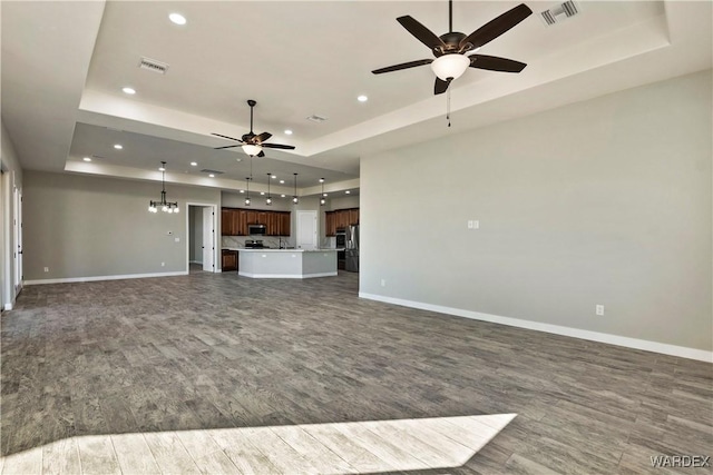 unfurnished living room with a raised ceiling, visible vents, and baseboards