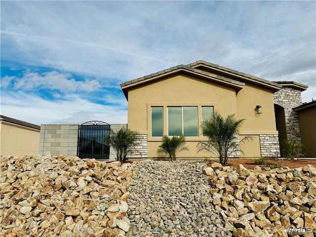 view of side of property featuring stone siding, a gate, and stucco siding