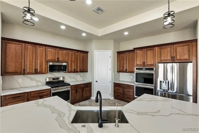 kitchen with appliances with stainless steel finishes, a sink, light stone counters, and pendant lighting