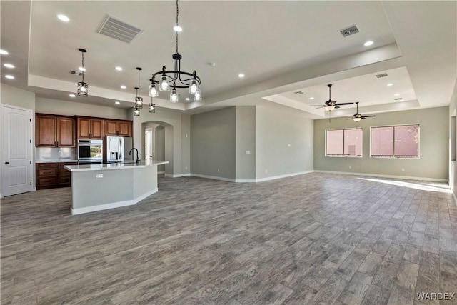 kitchen featuring decorative light fixtures, stainless steel appliances, a raised ceiling, open floor plan, and a kitchen island with sink